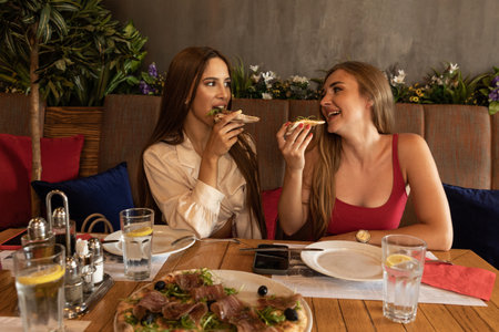 Two girlfriends eating pizza in the restaurantの写真素材