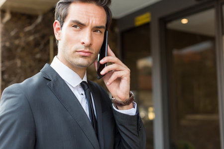 Handsome businessman in suit talking on the smartphone outdoorの写真素材