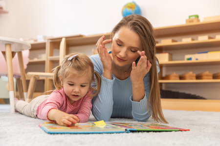 Mother and toddler daughter lying on the floor readingの写真素材