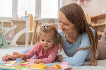 Mother and toddler daughter lying on the floor readingの写真素材