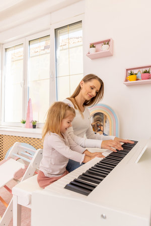Little girl playing a piano with her motherの写真素材