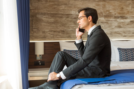 Businessman in suit talking on the mobile phone in his hotel room, bad newsの写真素材