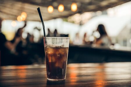 glass of cola with ice on a wooden table at an outdoor summer cafe. peoples on backgroundの写真素材