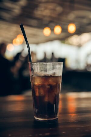 glass of cola with ice on a wooden table at an outdoor summer cafe. peoples on background. verticalの写真素材