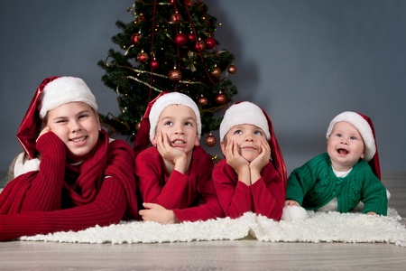 Four children in red hats are around Christmas tree.の写真素材