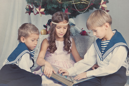 Three children are sitting around the Christmas tree, indoorの写真素材