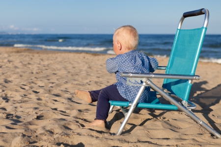 Happy small girl sitting on chair at beachの写真素材