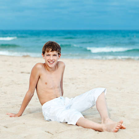 Portrait of teen sitting on sand near seaの写真素材