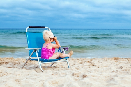 Happy small girl sitting on chair at beachの写真素材