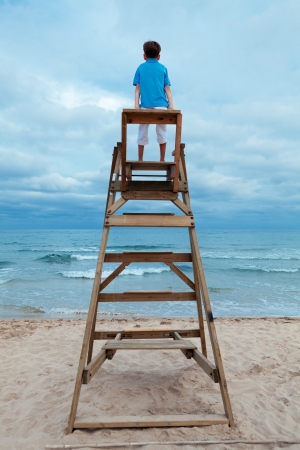 Boy sitting on lifeguard chair, outdoorの写真素材