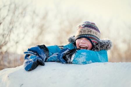 Happy child in winterwear laughing while playing in snowdrift outsideの写真素材