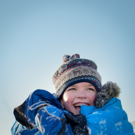 Happy child in winterwear laughing while playing in snowdrift outside