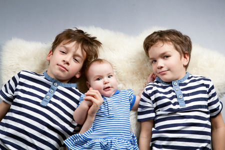 Portrait of happy brothers and cute small sister in sailor dress in studio on  gray backgroundの写真素材