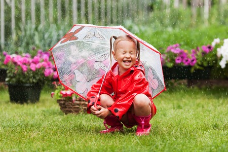 Happy fun pretty little girl in red raincoat with umbrella walking in park summer, ladybug costume, portrait, rain, outdoorの写真素材