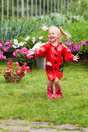 Happy fun pretty little girl in red raincoat with umbrella walking in park summer, ladybug costume, portrait, rain, outdoorの写真素材