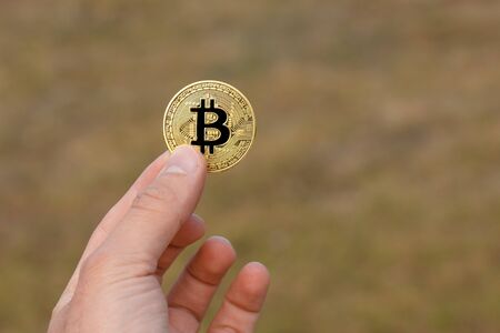 Man fingers are holding a big round golden bitcoin coin in front of yellow green pattern