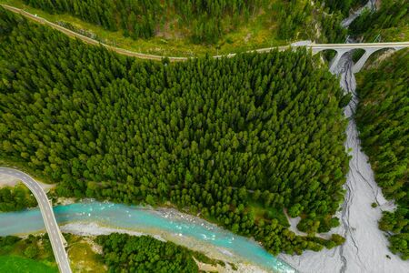 Inn River flowing in the forest in Switzerland. Aerial view from drone on an old railway bridge viaduct in the mountains.の写真素材