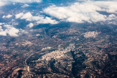 Aerial view from the plane on the panorama of the city through the clouds. View from above on the town near the mountains and hills ridge. View from above on mountain landscapeの写真素材