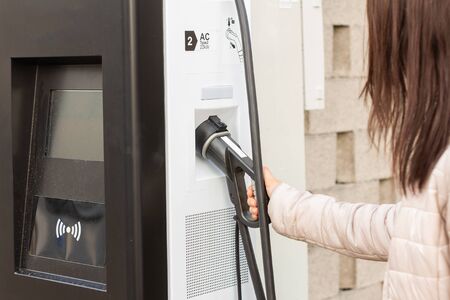 Woman use electrical fast charger to electrical or hybrid automobiles. High technology charger for...