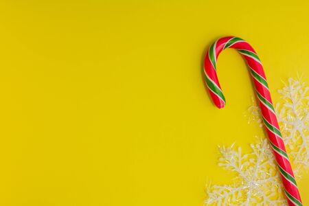 Traditional christmas caramel candy cane and snowflakes on a yellow background. Winter Holiday festive greeting card with copy space for the text. Xmas flat lay conceptの写真素材