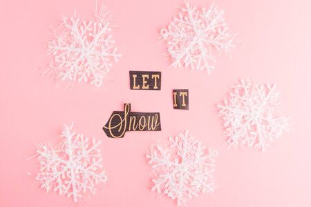Snowflakes on a pink background with Let It Snow lettering inscription. Winter Holiday festive greeting gift card. Xmas flat lay conceptの写真素材
