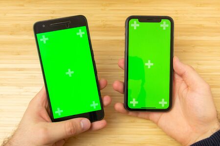 Mockup image of hands holding two black mobile phone with green screen on the office table on the backgroundの写真素材