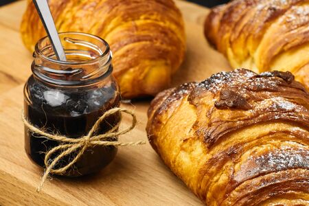 Freshly baked croissant with a berry jam in a jar on a wooden desk. French breakfast concept. Homemade pastry.の写真素材