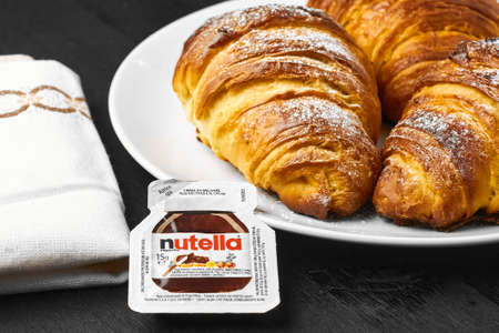 Freshly baked croissants with nutella on a white plate near serviette on a black background. Traditional french or italian breakfast. Homemade pastry.