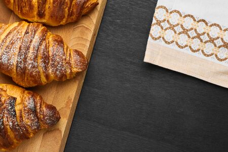 Traditional italian chocolate croissants on wooden board near serviette on a black background....