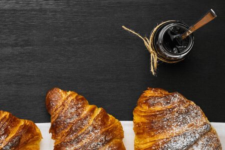 Top view of three croissants and a jar of jam on a black background with copy space.の写真素材