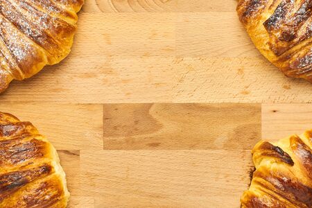 Croissants in the corners on a wooden desk with copy space in the middle.の写真素材