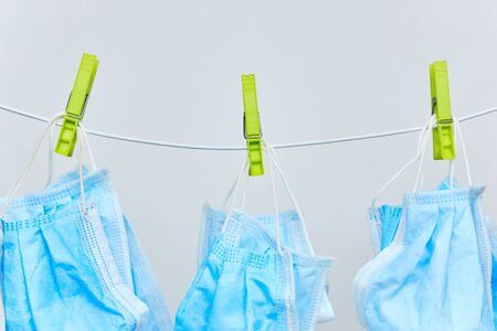 Drying of blue protective surgical masks on clothesline with green clothespins on a white...