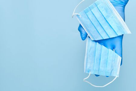 Mans hand in protective gloves holding a cut face mask on a blue back ground with copy space....