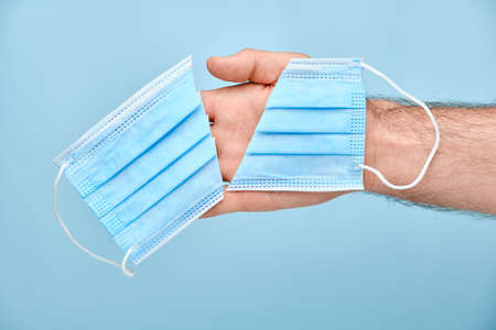 Man holding a cut mask on a blue background. Coronavirus, SARS-CoV-2 pandemic is over. End of...