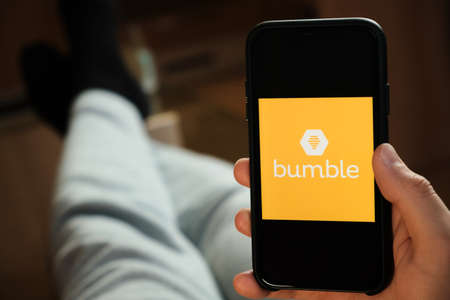 Bumble application on the smartphone in mans hand. Man laying and using application for dating and...