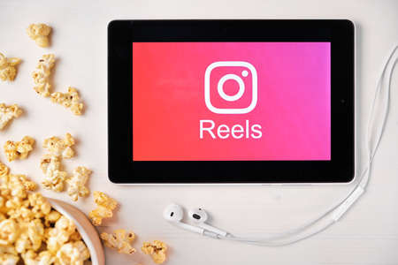 Reels logo on the screen of the tablet with popcorn box and Apple earphones on the background....