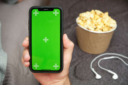 Close up mans hand holding a mobile phone with XXX logo with  earphones and popcorn box next to him, August 2020, San Francisco, USAの写真素材