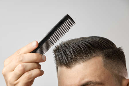 Close up young man combing his hair with a plastic comb. Styling hair after barbershop.の写真素材