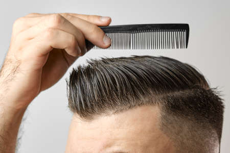 Close up young man combing his hair with a plastic comb. Styling hair after barbershop.の写真素材
