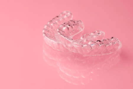 Two Invisible dental teeth aligners on the pink background. Orthodontic temporary removable braces...