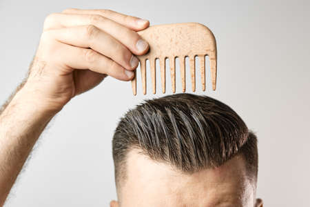 Man brushing his hair with a wooden comb and show how to take care about hair at home. Modern and...
