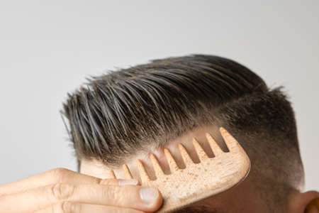 Close up man brushing his hair with wooden comb on the grey background. Treatment against hair lost and dandruff concept. Cosmetic products for men. Barbershop advertising.の写真素材