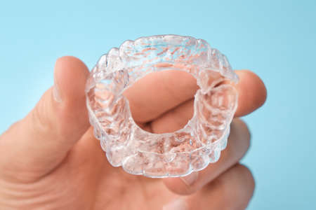 Close up mans hand holding invisible aligners for whitening and straightening of teeth on the blue...