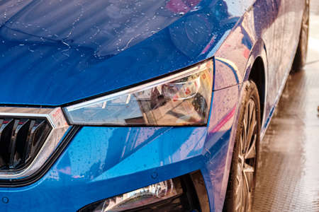 Close up hood and headlight of a blue car in a drops of water after car washing. Clean car after...