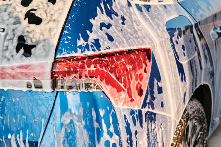 Close up a headlight in a soap during car washing with a foam. Cleaning a car using high pressure water.の写真素材