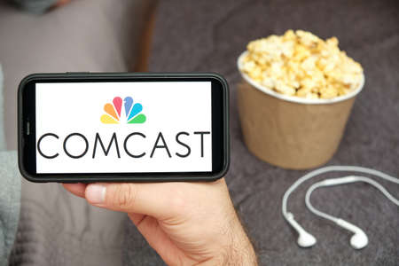 Foto de Comcast logo on the mobile phone screen with popcorn box and Apple earpods on the background. Leisure time at home concept. September 2020, San Francisco, USA - Imagen libre de derechos