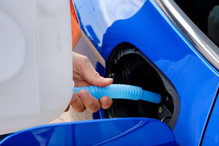 Close up filling of diesel exhaust fluid from canister into the tank of blue car for reduction of air pollution. Environmental or eco friendly solutionの写真素材