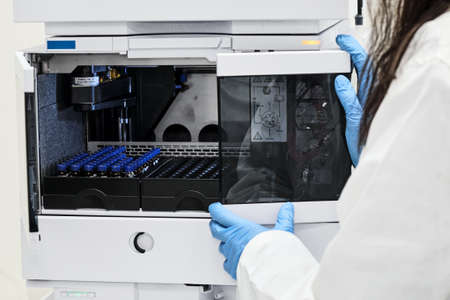 Close up scientist put sample in a glass vial with blue cap into the auto sampler rack in HPLC...