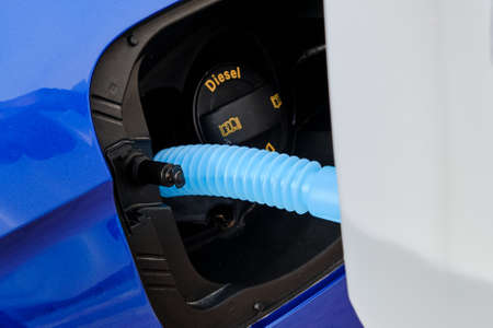 Close up filling of diesel exhaust fluid from canister into the tank of blue car for reduction of...