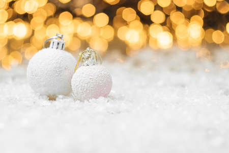 Decorative Christmas balls laying in a snow with yellow lights bokeh on the background. Greeting card for New Year holidays or party with copy space.の写真素材